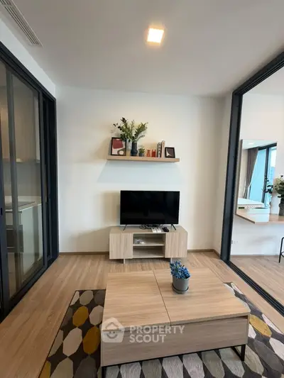 Modern living room with stylish decor and TV unit, featuring wooden flooring and glass doors.