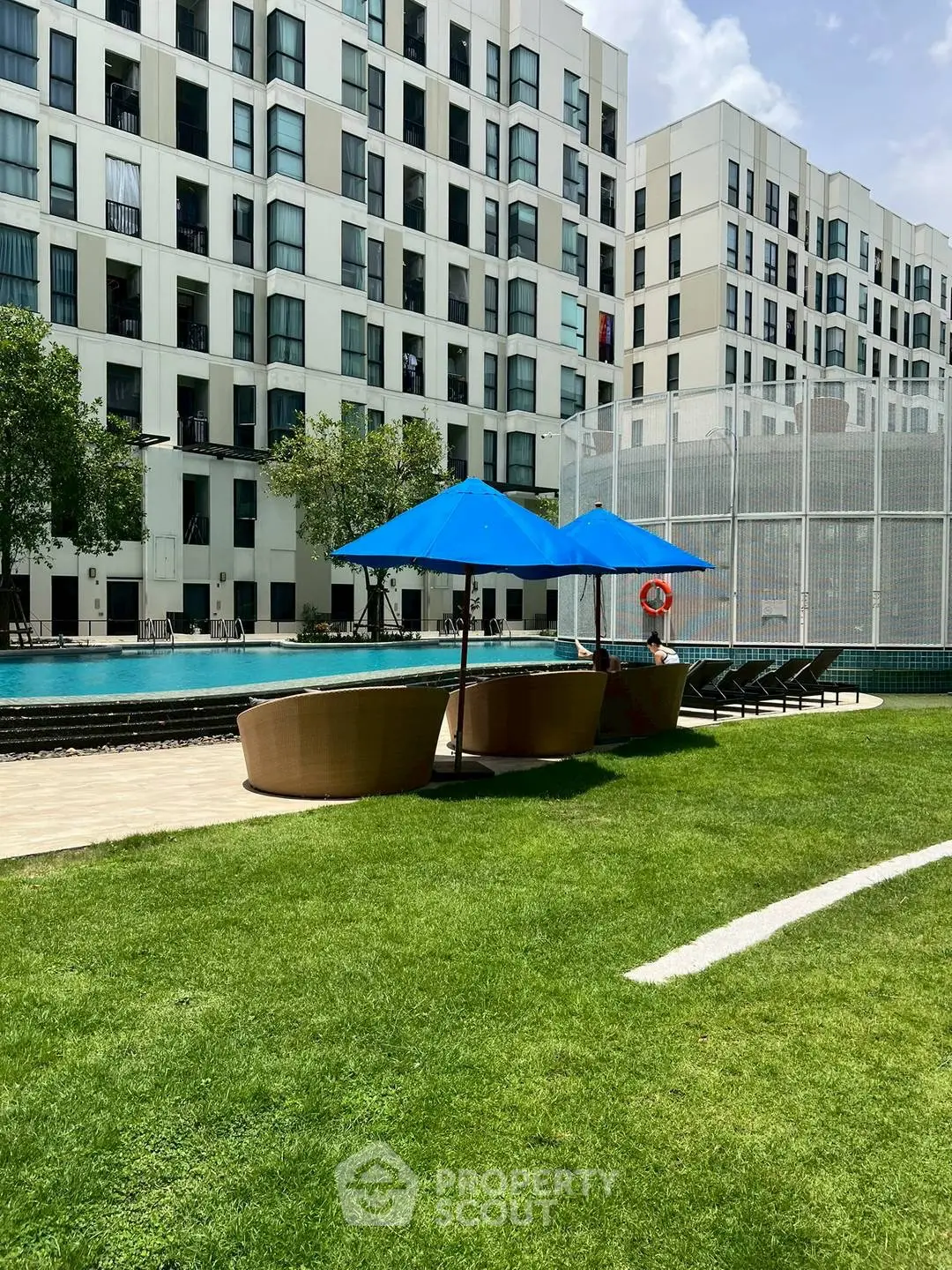 Modern apartment complex with poolside relaxation area and lush green lawn.
