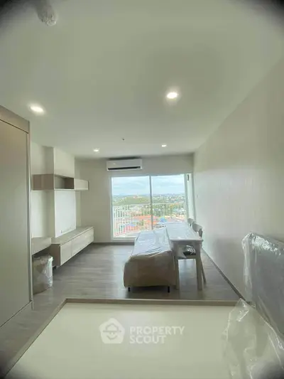 Modern living room with large window offering stunning city view, sleek furniture, and natural light.