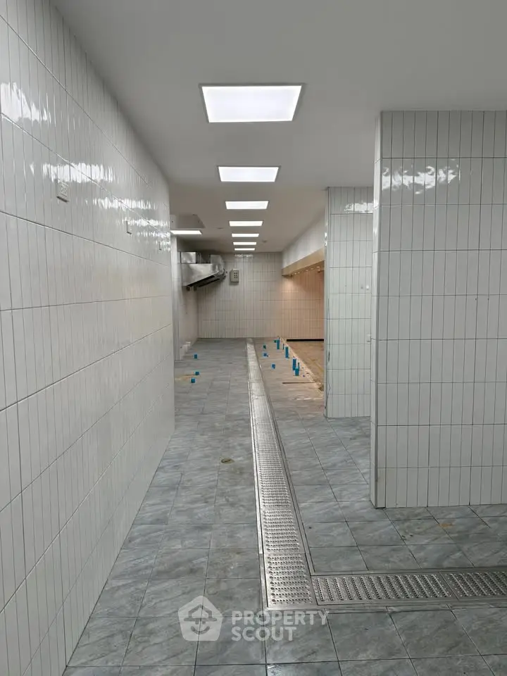 Spacious tiled commercial kitchen area with modern lighting and drainage system.