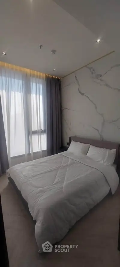 Modern bedroom with elegant marble accent wall and large window with sheer curtains.
