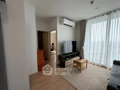 Modern living room with air conditioning and natural light, featuring a cozy seating area and a TV.