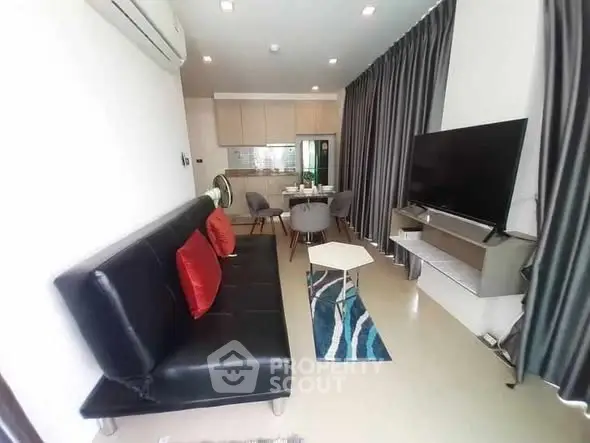 Modern living room with sleek black sofa and large TV, open to a stylish kitchen area.