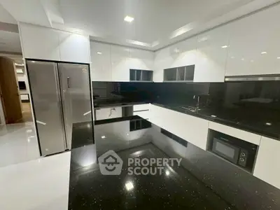 Modern kitchen with sleek black countertops and white cabinetry, featuring stainless steel appliances and built-in microwave.