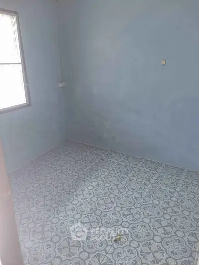 Empty room with patterned tile flooring and a window, ideal for customization.