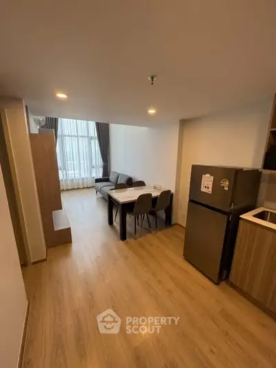 Modern open-plan living room with dining area and kitchen, featuring sleek furniture and natural light.