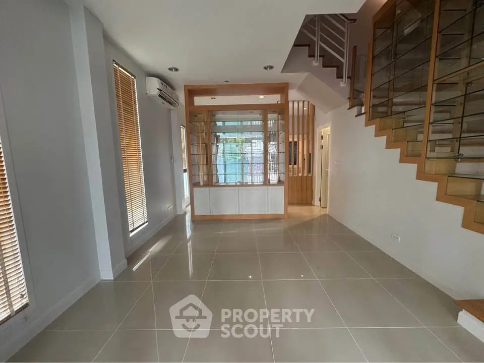 Spacious modern living room with sleek staircase and large windows in a contemporary home.