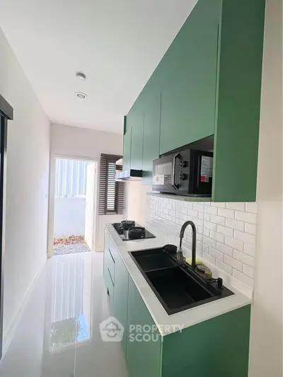 Modern kitchen with sleek green cabinets and gas stove in a bright, narrow layout.