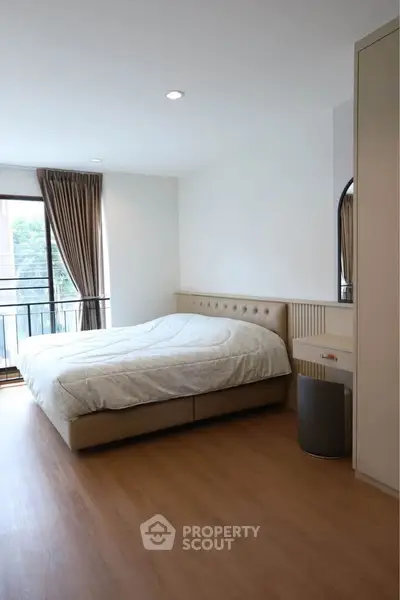 Spacious bedroom with large window and modern furnishings in a stylish apartment.