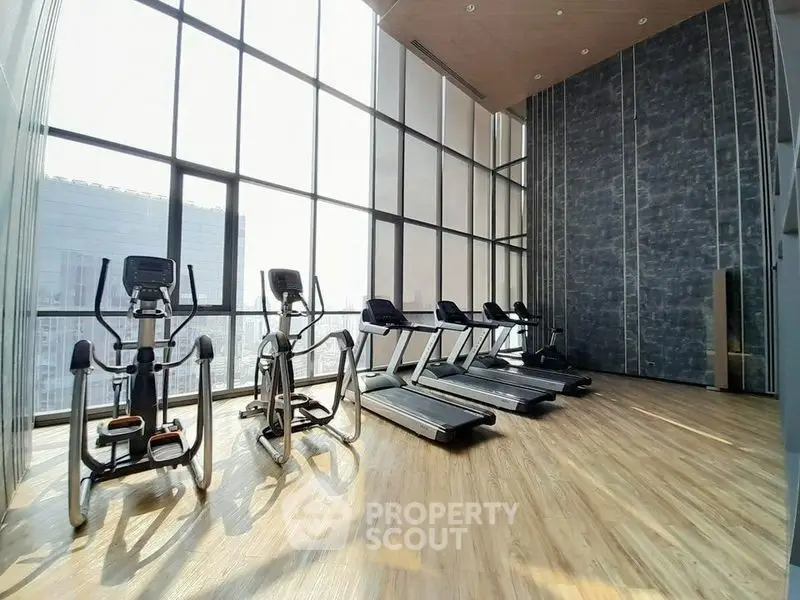 Spacious gym with modern equipment and floor-to-ceiling windows offering city views.