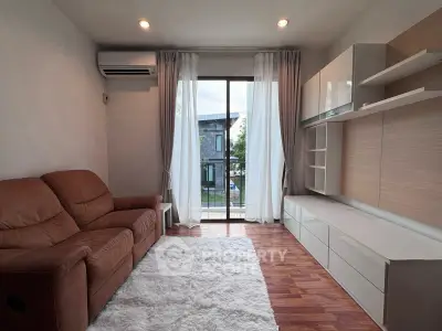 Cozy living room with brown leather sofa, modern shelving, and large window overlooking greenery.