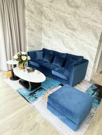Stylish living room with blue velvet sofa, modern coffee table, and elegant decor on a chic rug.