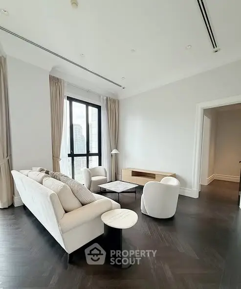 Elegant living room with modern furniture and city view, featuring dark wood flooring and large windows.