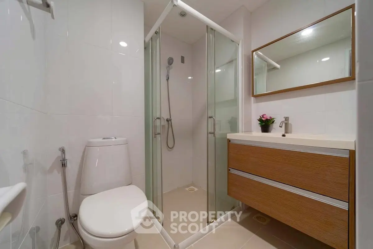 Modern bathroom with glass shower and wooden vanity in sleek design.