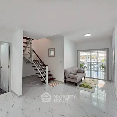 Modern living room with sleek staircase and large windows offering natural light.