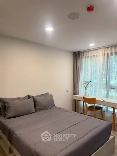 Cozy bedroom with modern decor and large window offering natural light.