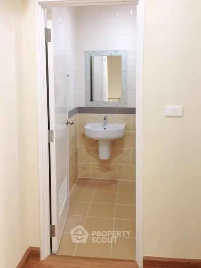 Compact bathroom with wall-mounted sink and mirror, beige tiles, and white door.