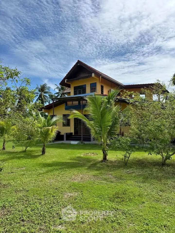 Charming yellow house with lush garden and tropical trees under a vibrant blue sky.
