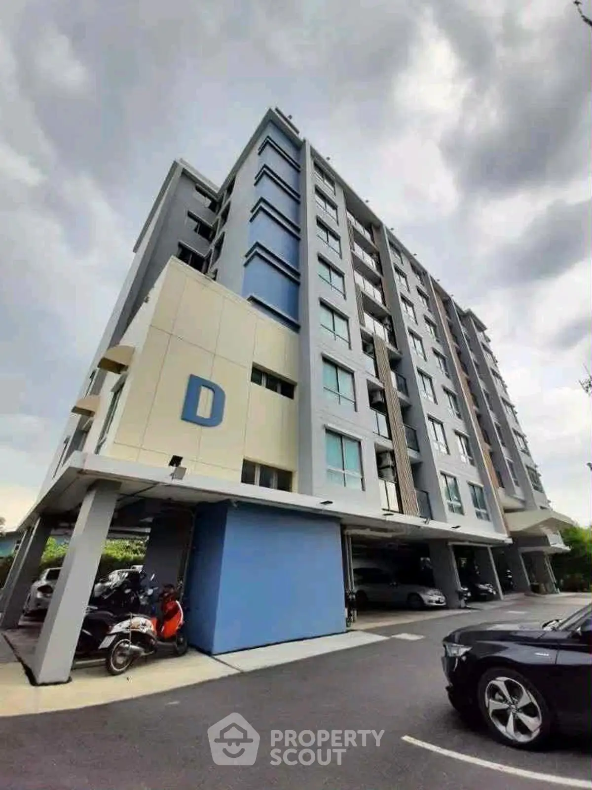 Modern multi-story apartment building with parking area and sleek design.
