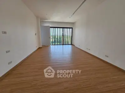 Spacious empty room with wooden flooring and large window offering natural light and scenic view.