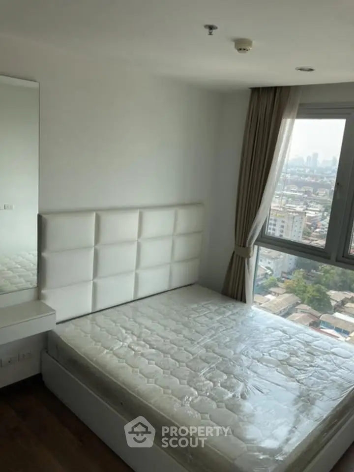 Modern bedroom with large window offering city views, featuring a stylish white bed and elegant decor.