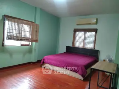Spacious bedroom with wooden flooring and natural light, featuring a comfortable bed and air conditioning.