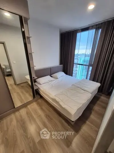 Modern bedroom with large window and city view, featuring stylish wooden flooring and cozy bedding.