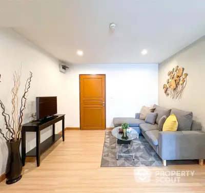 Spacious living room with elegant hardwood floors, cozy grey sofa set, and modern decor, perfect for comfortable urban living.