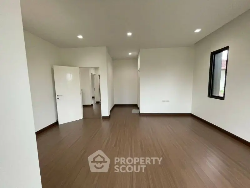 Spacious empty room with wooden flooring and white walls, ideal for customization.