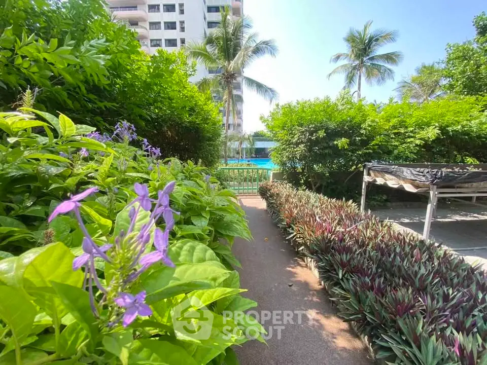 Lush garden pathway leading to a pool in a tropical residential complex.