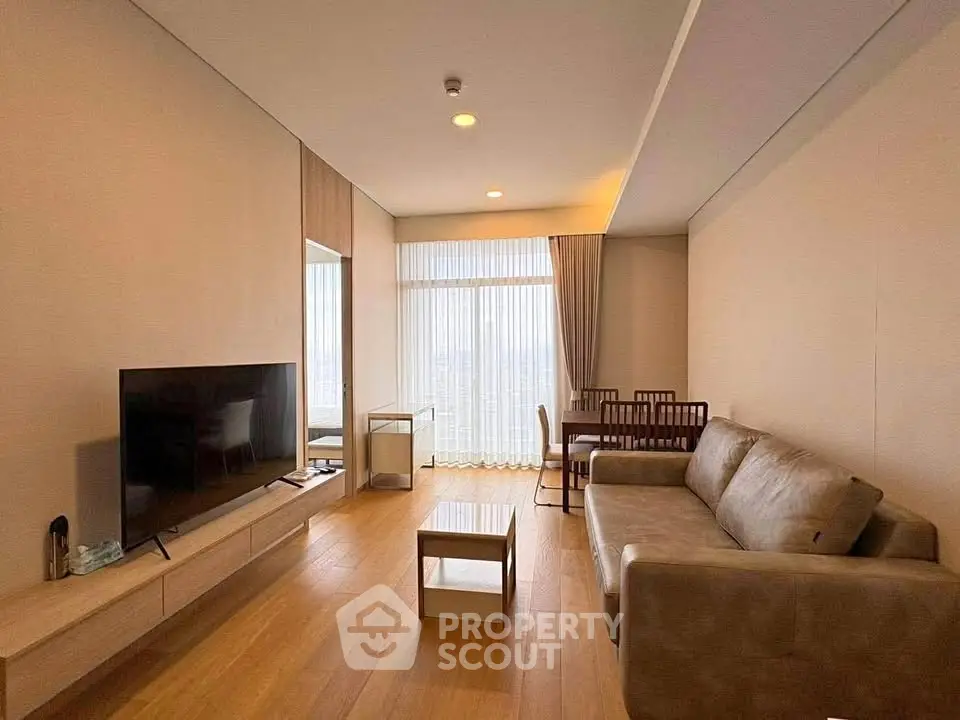Spacious modern living room with large TV and elegant furniture, featuring floor-to-ceiling windows.
