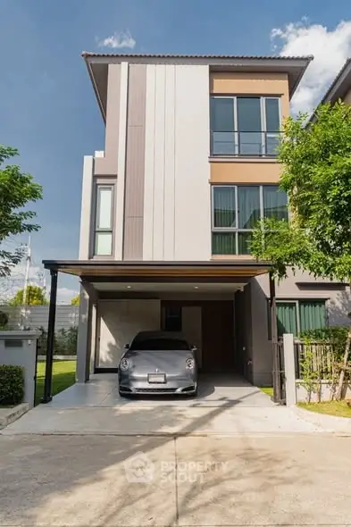 Modern three-story house with carport and sleek design in a sunny neighborhood.