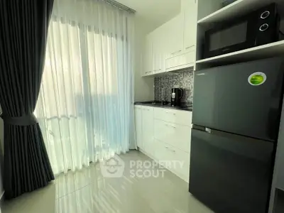 Modern kitchen with sleek cabinets, fridge, and microwave, featuring elegant floor-to-ceiling curtains.