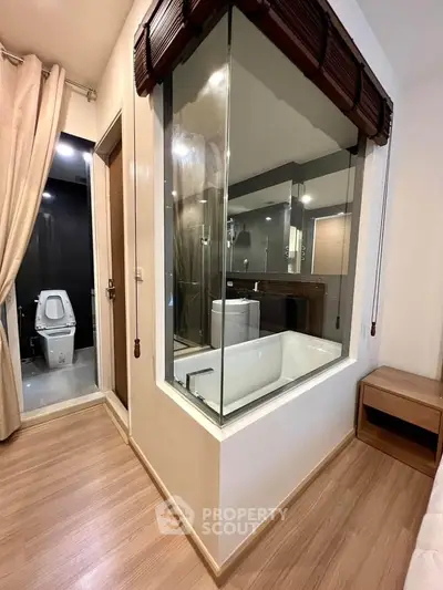 Modern bedroom with glass-walled bathroom featuring a bathtub and wooden flooring.