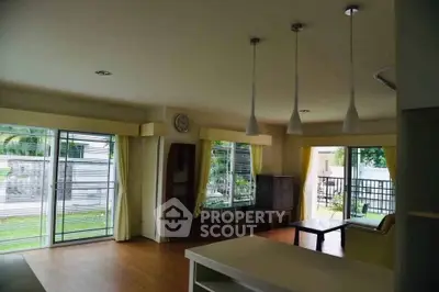 Spacious living room with large windows and garden view, featuring modern lighting and wooden flooring.