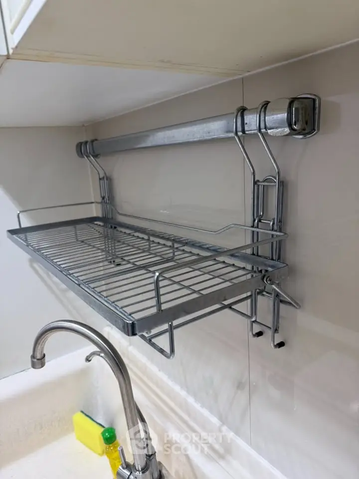 Modern kitchen with sleek metal dish rack above sink, showcasing efficient use of space.