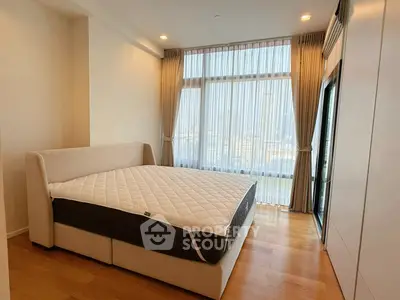Spacious bedroom with large window and elegant curtains, featuring a comfortable bed and wooden flooring.