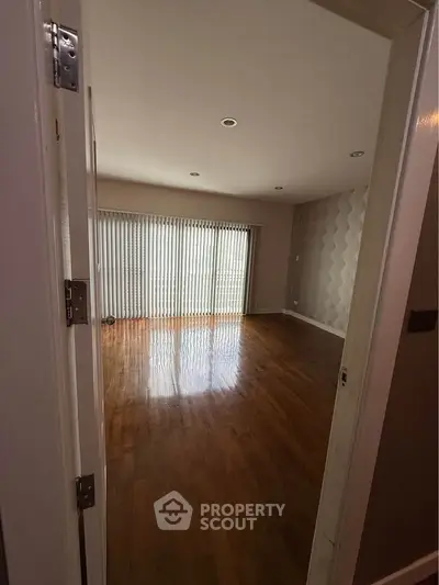 Spacious empty room with wooden flooring and large window blinds, perfect for customization.