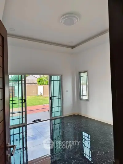 Spacious room with glossy black flooring and sliding glass doors opening to a garden view.