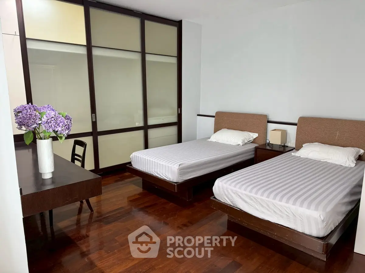 Spacious bedroom with twin beds and elegant wooden flooring, featuring a stylish desk and vibrant floral decor.
