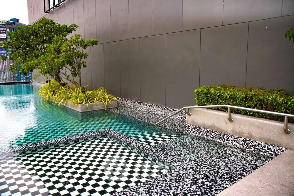 Luxurious modern swimming pool with stylish mosaic tiles and lush greenery in a high-end residential complex.