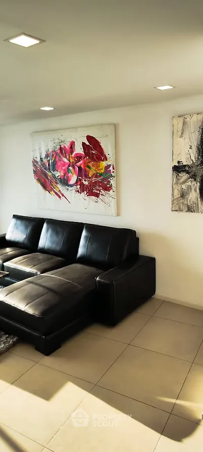 Modern living room with black leather sofa and vibrant abstract art on white walls.