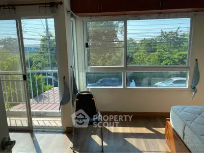 Bright bedroom with balcony access and large windows overlooking greenery.