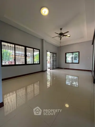 Spacious empty living room with large windows and ceiling fan, perfect for customization.