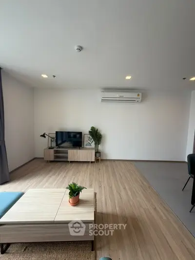 Modern living room with wooden flooring and air conditioning, featuring a TV and stylish furniture.