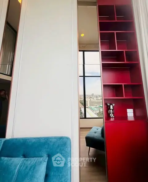 Modern apartment interior with vibrant red shelving and plush blue seating, offering a stunning city view.
