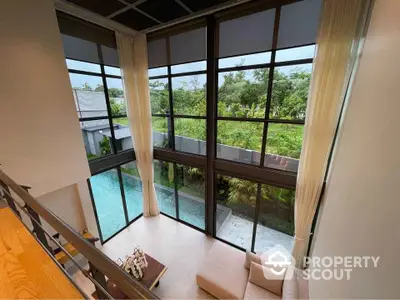 Luxurious living room with floor-to-ceiling windows overlooking a serene pool and lush greenery.