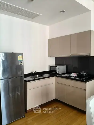 Modern kitchen with sleek cabinets, stainless steel fridge, and wooden flooring in a stylish apartment.