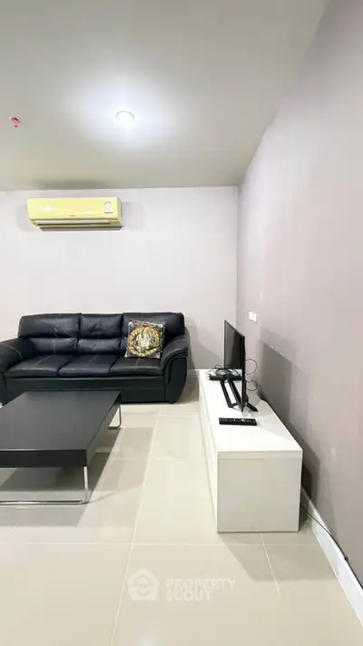 Modern living room with sleek black sofa, air conditioning, and minimalist decor.