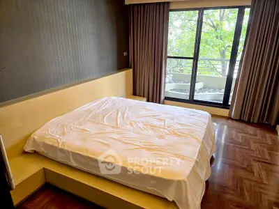 Spacious bedroom with large window and balcony access, featuring elegant wooden flooring.